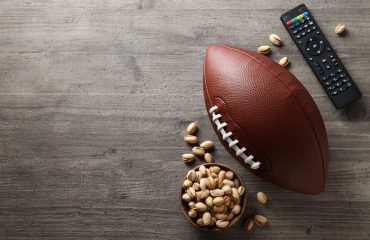 Football, Remote, and a bowl of pistachios on grey background