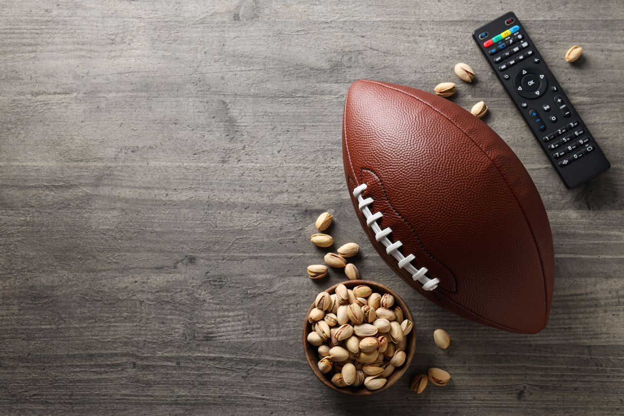 Football, Remote, and a bowl of pistachios on grey background